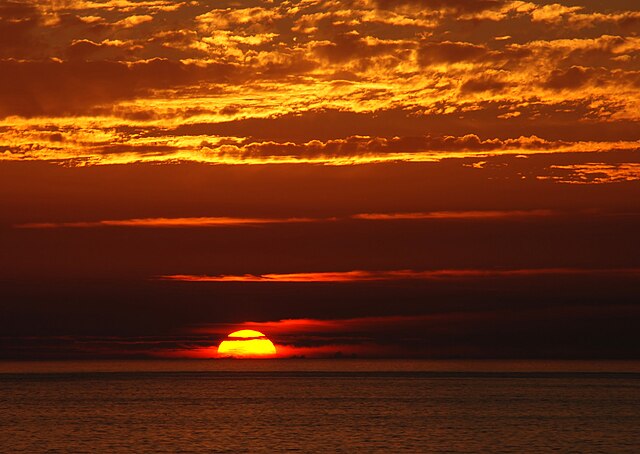 A sun hanging low on the horizon, creating an deep orange sunset behind clouds.