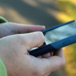 A man's hands holding a smartphone. The background is a blurry green.