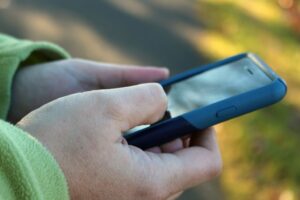 A man's hands holding a smartphone. The background is a blurry green.